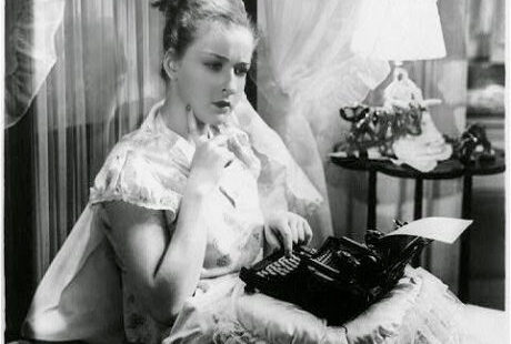 women in bed writing on typewriter